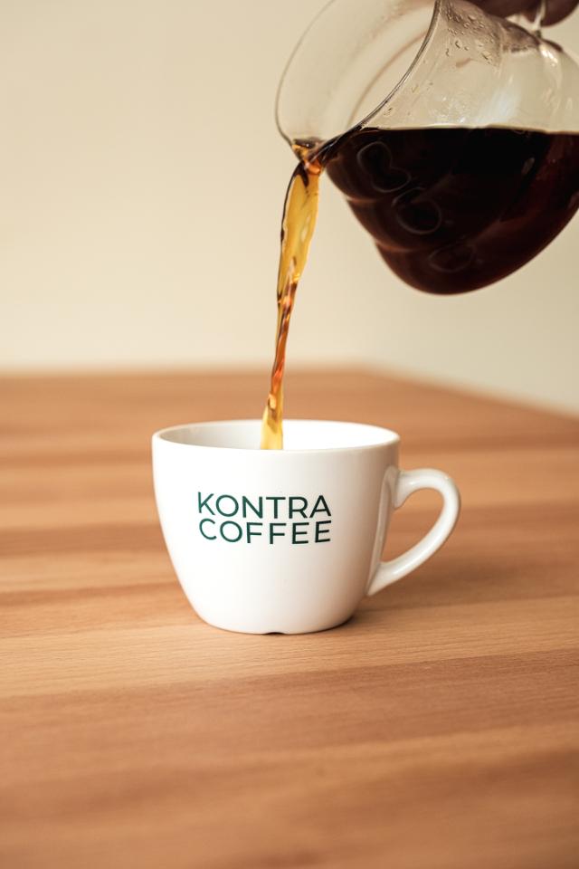 kaffe haeldes fra hario glaskande ned i kop med kontra coffee logo