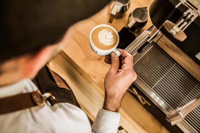 barista har brygget en kop kaffe med latteart paa toppen