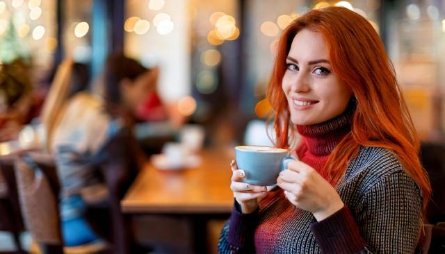 kvinde holder en blaa kaffekop kigger ind i kameraet og smiler